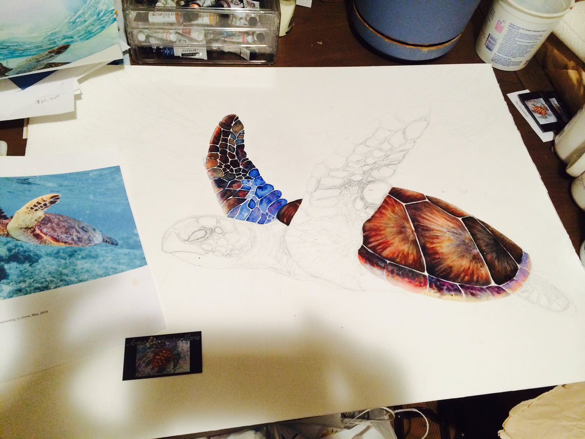 Aloha Spirit watercolor in progress showing layered transparent glazing a partially completed sea turtle drawing, with color reference photos of a sea turtle placed nearby. Artist Christie's workspace with art supplies on art table.
