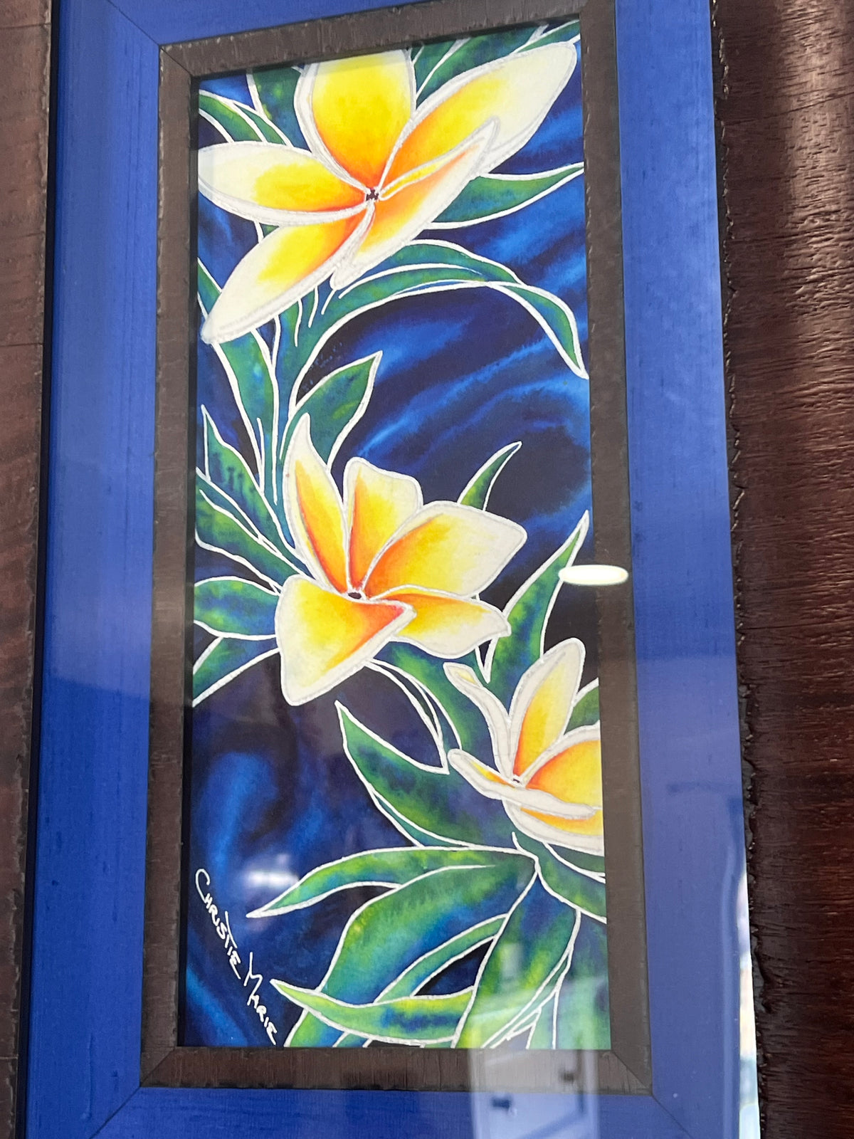 Wedding Lei photographed in its actual custom frame, showing the depth of the dark wood molding and blue silk liner from an angle.