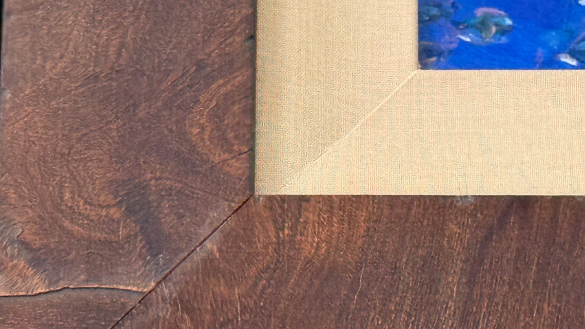Close-up of the textured dark wood frame and tan silk-covered liner on Peace of the Tropics